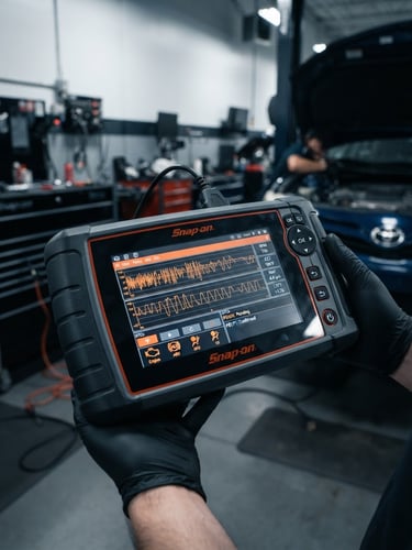 Sharp industrial photography, crisp cool studio lighting, high contrast charcoal and orange tones, macro technical detail of a diagnostic scanner screen showing active data in a clean professional garage bay, 50mm lens