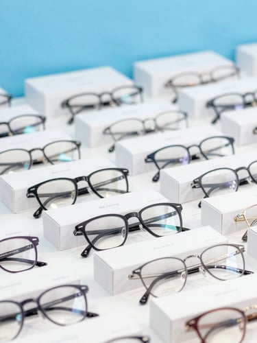 Crisp daylight shot, neatly packed white boxes of eyewear inventory on a sorting table, clean sky blue accents, 50mm lens