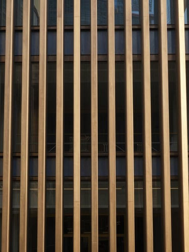 A close-up of a structured bronze facade with clean vertical lines, warm sand tones, indirect natural daylight, reflecting stability and order, 35mm.