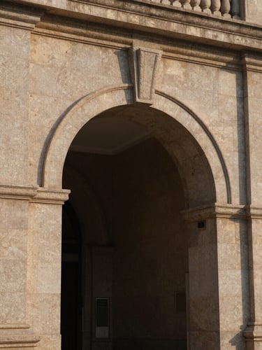 Architectural detail of a massive stone archway, strong shadows, warm afternoon light reflecting on structured granite, elegant and protective, 35mm.