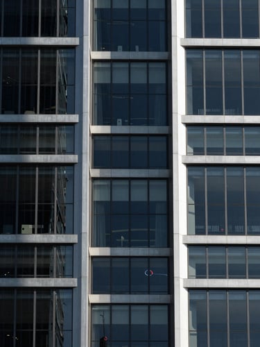Symmetrical modern skyscraper facade with clean glass panels casting sharp geometric shadows under high-contrast sunlight, 85mm architectural photography.