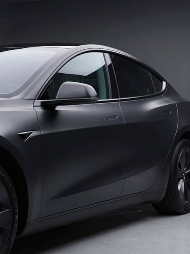 Low-angle heroic shot of a matte black Tesla Model S parked in a high-contrast studio, sharp laser-like cool-toned rim lights reflecting off the side window glass, ultra-sharp focus, 85mm
