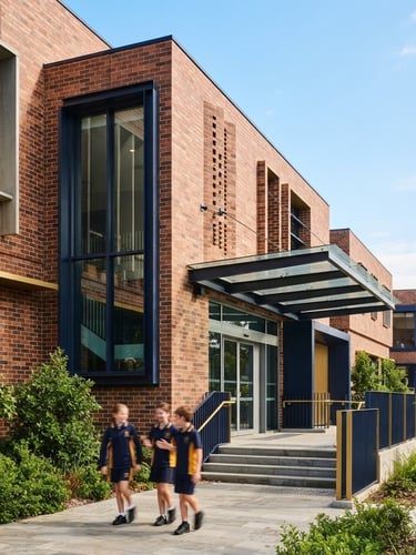 Bright editorial photography of the modern brick facade of The Huda Public School under clear blue skies, clean architectural lines, warm daylight, shallow depth of field