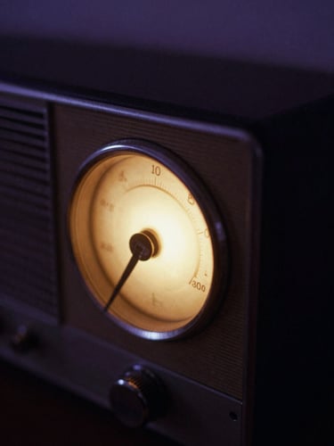 Close-up of vintage analog radio dial glowing softly in a dark room, warm amber light, deep violet shadow tones, atmospheric film photography