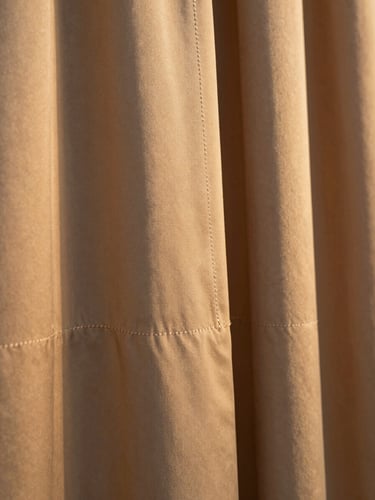 Editorial close-up of a high-quality heavy silk garment hem, warm golden-hour side-light highlighting the precise stitching and premium texture