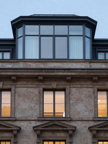 Architectural detail of a historical building facade with modern glass penthouse extension on top, contrasting heritage stucco and clean steel lines, blue hour lighting