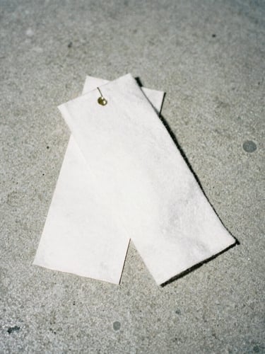 Medium close-up of heavy cotton garment tags on a raw concrete background, direct harsh flash lighting, high contrast, desaturated tones, 35mm film