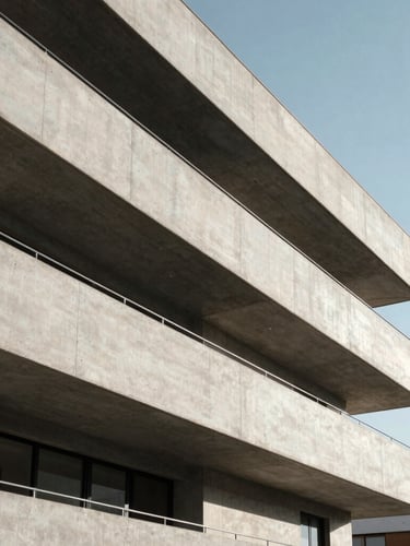 Strict geometric composition of a modern residential building facade in Spain, sharp concrete lines, deep architectural shadows under bright daylight, clean sky.