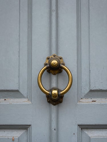 Close documentary shot of a worn front door with peeling paint and a tarnished brass knocker, natural overcast light, honest architectural detail, no staging