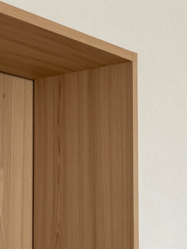 Close-up architectural shot of bespoke oak wood joinery meeting a textured plaster wall, perfect alignment, soft side lighting, editorial design detail