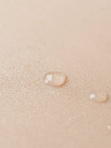 Close-up of clean skin showing natural texture with water droplets, soft diffused natural daylight, warm sand tones, minimalist composition, macro photography