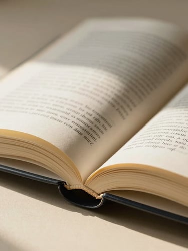 Close-up macro detail of a beautifully typeset open book on a warm cream surface, soft natural side-lit daylight casting elegant shadows, paper texture visible.