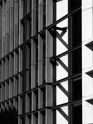 Minimalist architectural photography of a modern concrete and steel corporate headquarters facade, sharp geometric shadows cast by harsh direct sunlight, high contrast charcoal and white tones, sharp focus, 35mm lens