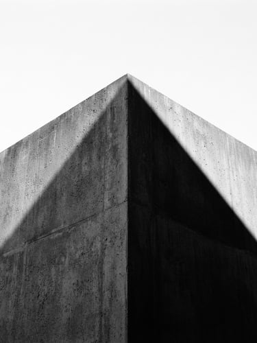 Minimalist architectural photography of a sharp concrete corner against a stark white sky, harsh direct sunlight casting a sharp black diagonal shadow, 35mm lens