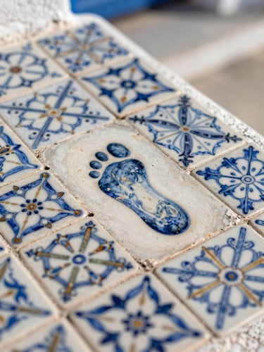 Close detail of hand-painted ceramic tiles on a Greek island doorstep, worn at the centre from decades of footfall, natural overhead daylight, shallow depth of field on the pattern edge