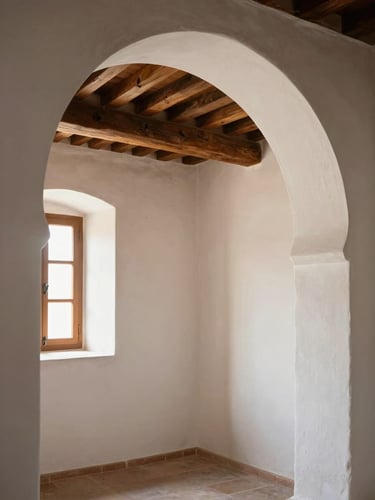 Interior arch of a whitewashed Andalusian room, a single wooden beam crossing the ceiling, warm afternoon light entering from a narrow window off-left, bare walls with faint texture of old lime plaster
