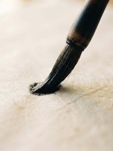Extreme close-up of a bamboo brush tip loaded with wet black ink touching textured warm Xuan paper, soft natural daylight, shallow depth of field.