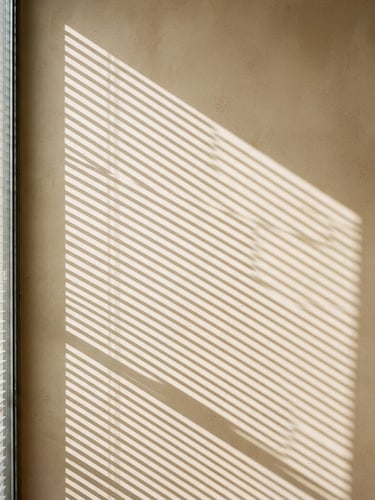 Minimalist architectural photography of elegant blinds casting geometric shadows on a warm plaster wall, bright natural daylight, neutral warm tones, 35mm