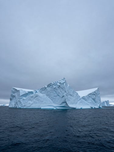 A towering monolithic iceberg in a dark blue arctic ocean, sharp edges, cold overcast daylight, cinematic wide-angle shot