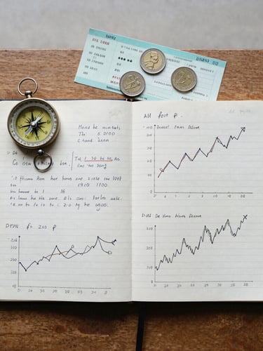 A top-down flat lay of a worn paper notebook filled with handwritten economic charts, next to a vintage compass, a train ticket, and local coins on a wooden table, natural overcast daylight, 35mm film grain