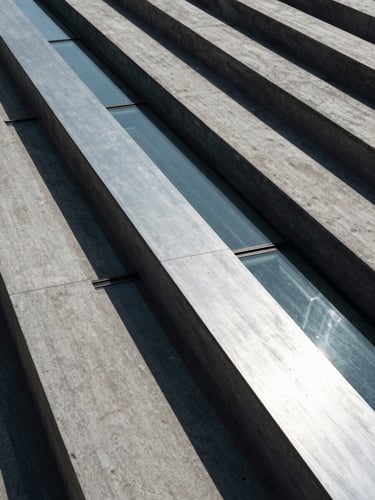 High-angle architectural perspective of concrete and glass lines, cool-toned lighting with sharp silver reflections and deep shadows, structural integrity.