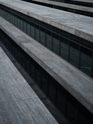 Wide panoramic high-angle architectural perspective of concrete and glass lines, low-key cool-toned lighting, deep graphite shadows.