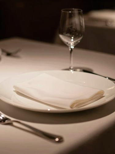 Elegant macro shot of a pristine, minimalist table setting in a luxury restaurant, low-key dramatic warm lighting, deep rich tones, 35mm.