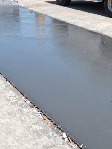 Low-angle sharp industrial photograph of a newly poured concrete driveway reflecting bright Texas sunlight, crisp steel-blue tones, 35mm lens