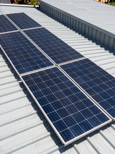 High-angle shot of clean solar panels installed on a modern industrial metal roof in Colombia, bright direct midday sunlight, sharp geometric shadows, high-contrast technical framing.