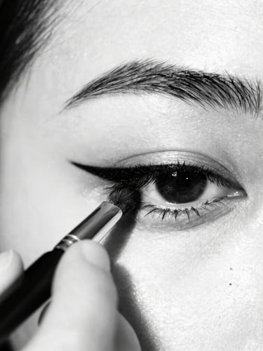 Extreme close-up of a makeup artist's hands applying sharp black eyeliner with a fine brush on a model's eye, high-contrast studio strobe lighting, deep blacks and pure whites, razor-sharp focus, 35mm, portrait aspect