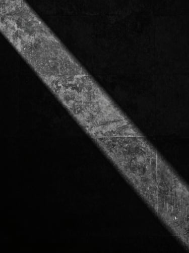 Abstract dark architectural photography of a monolithic black concrete wall, sharp directional light casting dramatic shadows, high-contrast monochrome, 35mm.