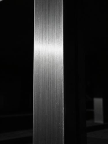 Extreme close-up of a heavy brushed steel structural column, dramatic chiaroscuro lighting, deep shadows, sharp focus, 35mm