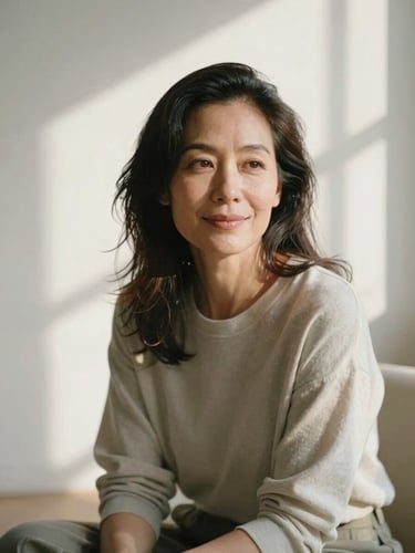 A medium close-up of Gaby Mol, a mature woman with a warm, serene expression, sitting in a sunlit studio with soft morning window shadows, earthy sage and cream tones, shallow depth of field, 35mm film texture.