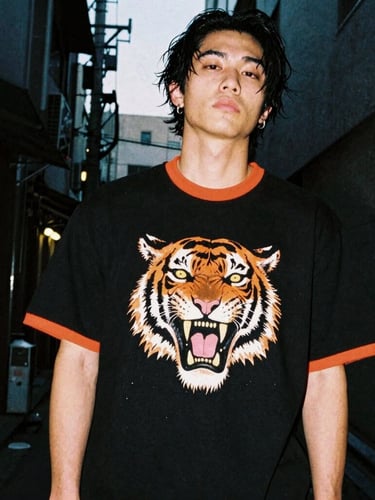Low-angle heroic shot of a streetwear model in a dark Tokyo alley at dusk, wearing a heavy-weight black tiger-graphic t-shirt, neon orange rim light, high contrast, 35mm film.