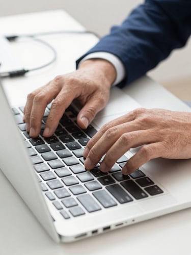 Close-up of hands working on a laptop keyboard, clean modern desk, bright daylight, subtle network cables in the background.