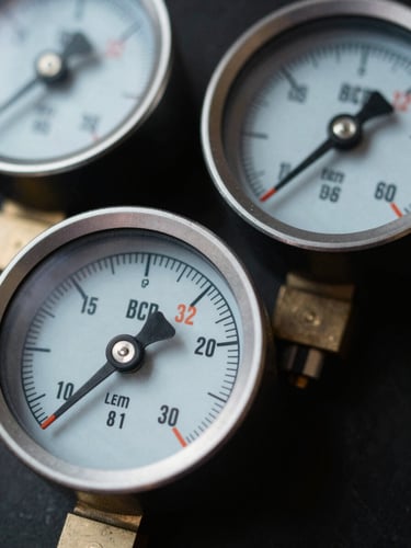 Macro close-up of digital manifold gauges showing precise pressure readings, sharp natural work-light, high-contrast cool tones with safety-orange accents, 35mm.