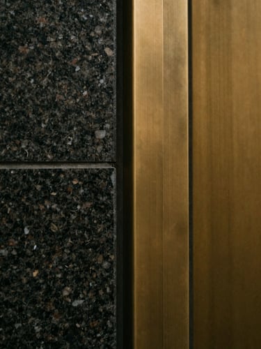 Minimalist close-up of high-quality dark granite and brushed brass materials, soft warm light reflecting off clean edges, architectural detail, 35mm film.