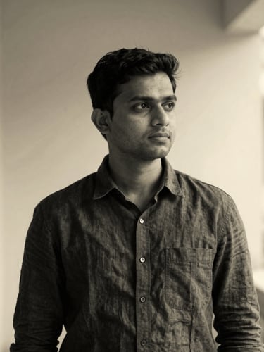 A professional, high-contrast black and white portrait of a thoughtful South Asian male engineer in a charcoal linen shirt, soft natural side lighting, negative space to the right.