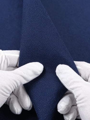 Macro close-up shot of hands in white gloves inspecting a roll of tightly woven navy fabric, showing texture and thread count, under bright studio lighting, clean and precise.