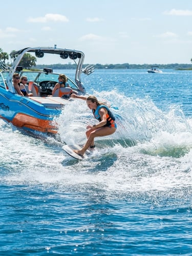 Dynamic low-angle action shot of a wakesurfer carving hard close to the transom of a MasterCraft boat, high-shutter-speed capturing crisp water spray in the midday Florida sun, vibrant blue water.
