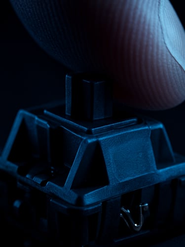 Extreme macro studio photograph of a mechanical keyboard switch being pressed by a finger, dramatic high-contrast lighting with deep blue shadows, sharp focus on the metallic contact points