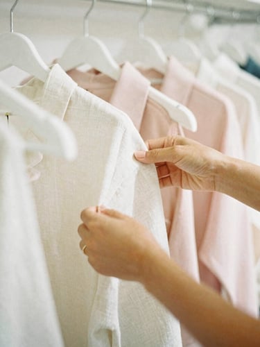 Intimate close-up of hands arranging soft linen apparel on a hanger in a sun-drenched boutique studio, warm Florida light casting soft shadows, 35mm