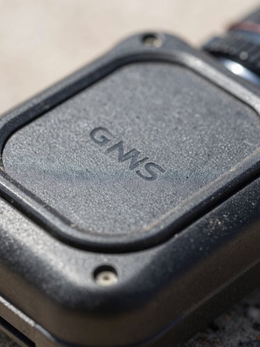 Macro details of ruggedized GNSS receiver casing, dust visible on the protective rubber seal, harsh high-contrast natural daylight, 35mm lens