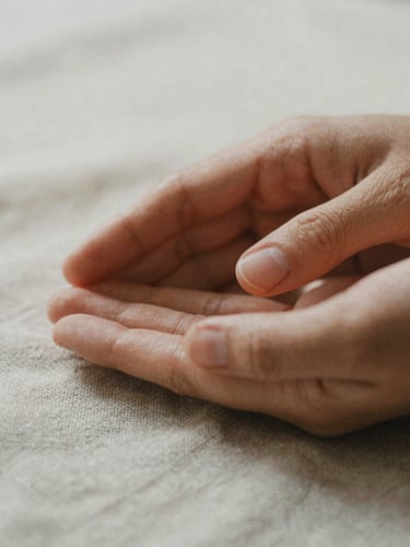 Macro close-up of warm hands gently hovering over textured organic linen, soft diffused morning light, shallow depth of field, 35mm film texture.