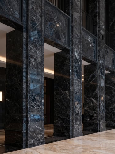 Sharp architectural photography of a luxury hotel lobby with dramatic high-contrast lighting, deep navy and charcoal tones, crisp marble columns, 35mm lens