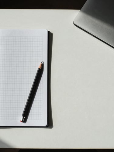 Overhead flat lay of a studio desk in north-facing daylight — a printed grid sheet, a pencil, and a closed notebook on cool off-white surface, sparse arrangement with generous empty space to the right
