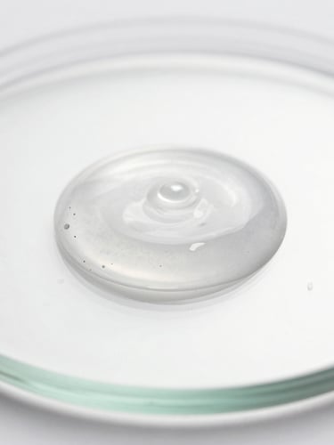 Macro lens close-up of a clear silky emulsion droplet on a clean glass plate, high-key crisp studio lighting, soft silver reflections, bright clean shadows.