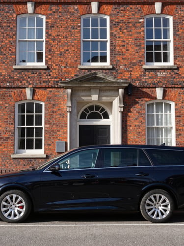A polished black executive transport vehicle parked in front of a historic brick building in Portsmouth, crisp morning daylight, sharp focus