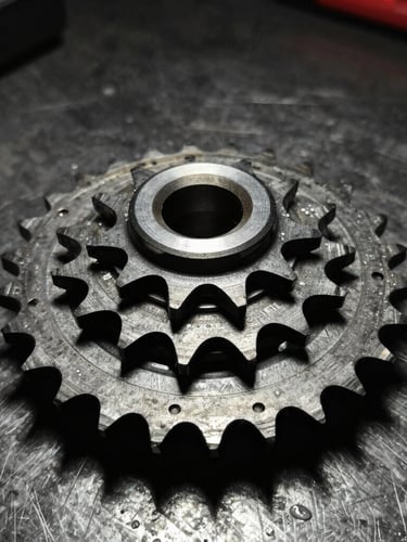 Macro close-up of a pristine, new metallic motorcycle gear set resting on a dark textured steel workbench, dramatic side-lighting highlighting precision teeth, 50mm lens