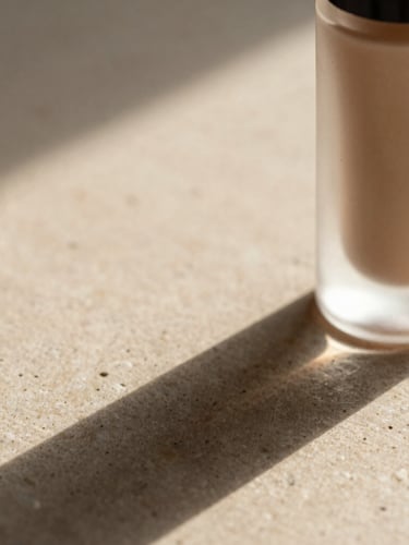 Extreme close-up of a single textured cosmetic bottle casting long, soft architectural shadows on a raw matte stone surface, diffused morning light, warm oatmeal tones, negative space on the left